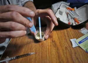 An addict prepares heroin, placing a fentanyl test strip into the mixing container to check for contamination.