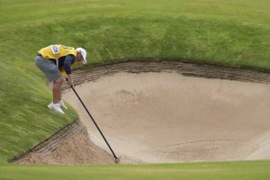 Jason Reynolds, caddie for Dean Burmester of South Africa, rakes a bunker on the 1st hole after Burmester played a shot from it during the third round of the British Open on Saturday.