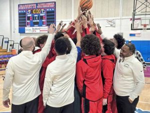 Jeannette boys basketball coach Adrian Batts (far right) joins his team in a huddle during a WPIAL championship ring ceremony Wednesday night at Jeannette High School. (Bill Beckner Jr. | TribLive)